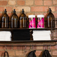 Shelf with bottles, scrummi waffle towels, and scrummi hair colour removal wipes against a brick wall.