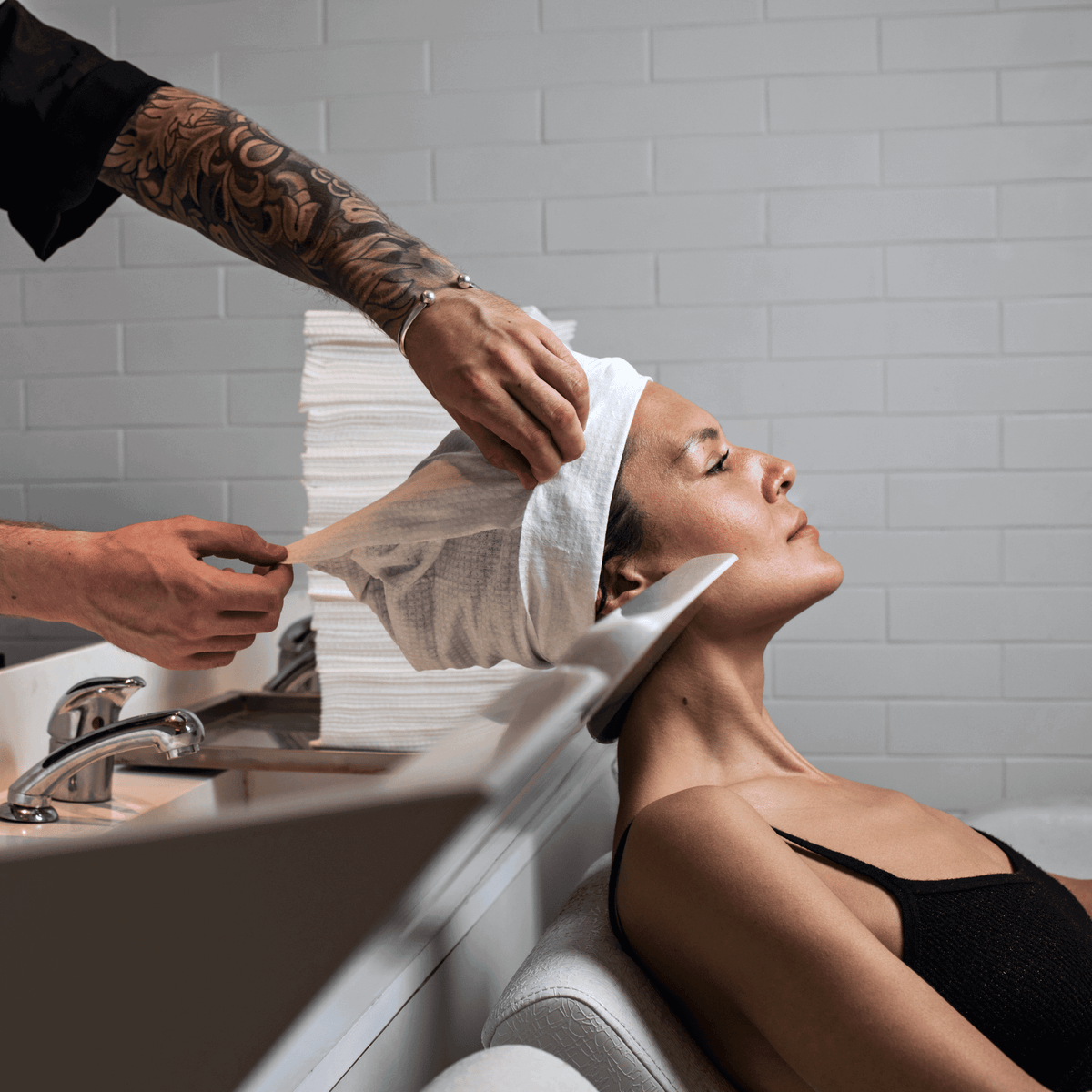 Image of Scrummi Hair Towel - LUXE in white being used to wrap and dry a client's hair in a salon. The towel’s textured waffle soft material are visible, providing effective drying and comfort. The disposable and biodegradable nature of the salon