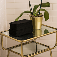 Image of a stack of Original Waffle Hand Towels in black, neatly organised in a salon. The towels feature a textured waffle weave and soft material, ready for use. The disposable and biodegradable qualities of the towels are highlighted, emphasising their